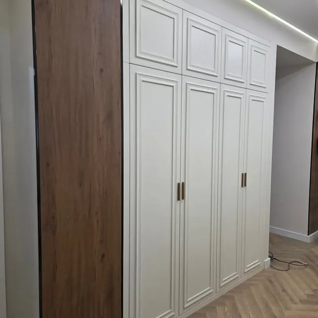 Белые распашные шкафы до потолка с рамочными фасадами и боковой панелью под дерево