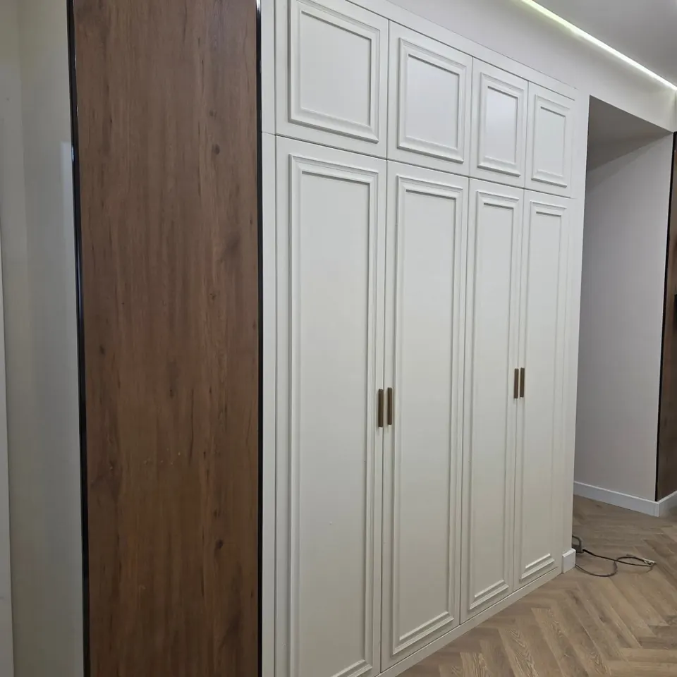 Белые распашные шкафы до потолка с рамочными фасадами и боковой панелью под дерево